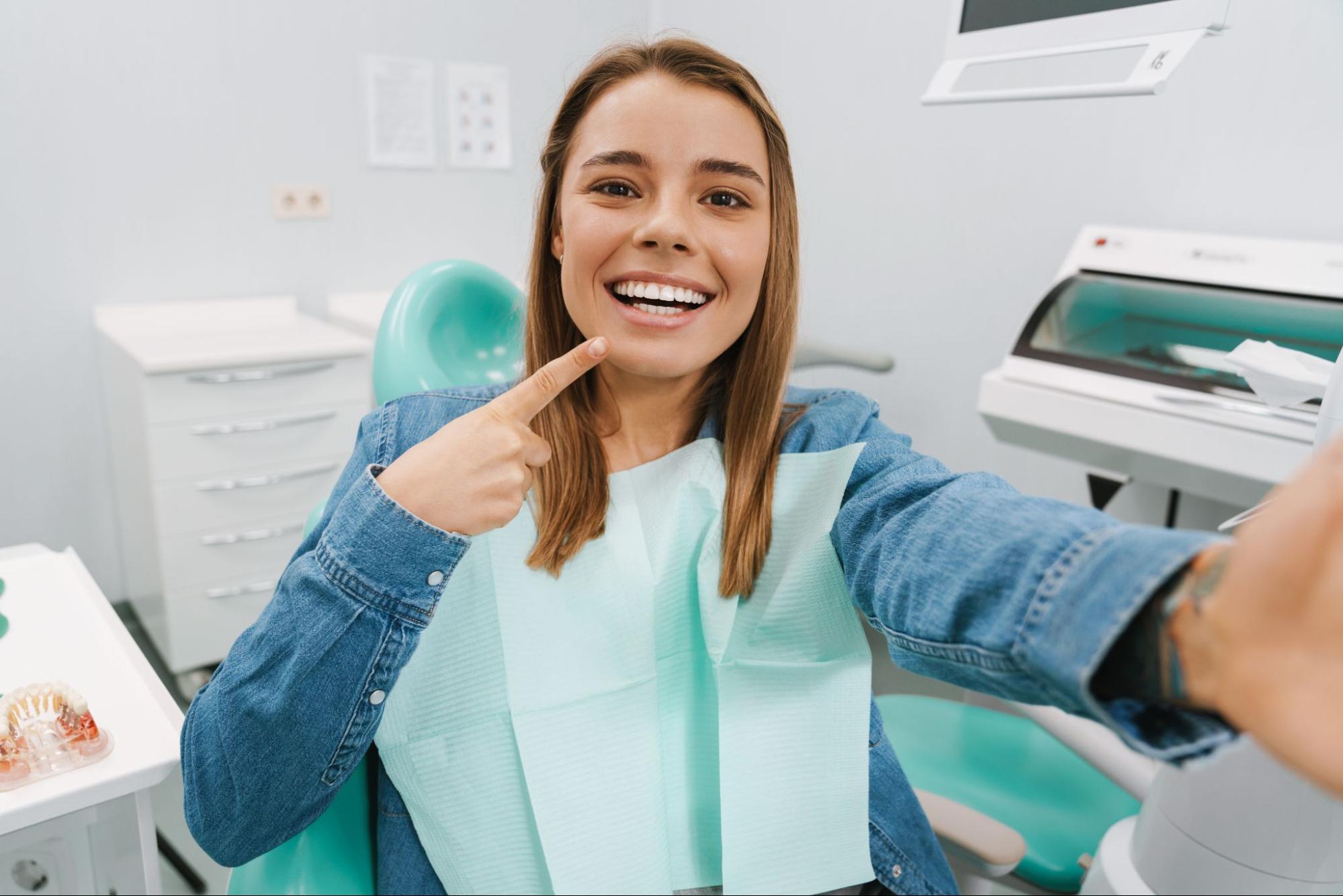 Woman pointing to her white smile while sitting in a dentist chair.