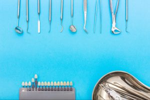 Top view of essential dental tools, including dental crown samples, a stainless tray with extraction instruments, and other popular tools for dentistry.