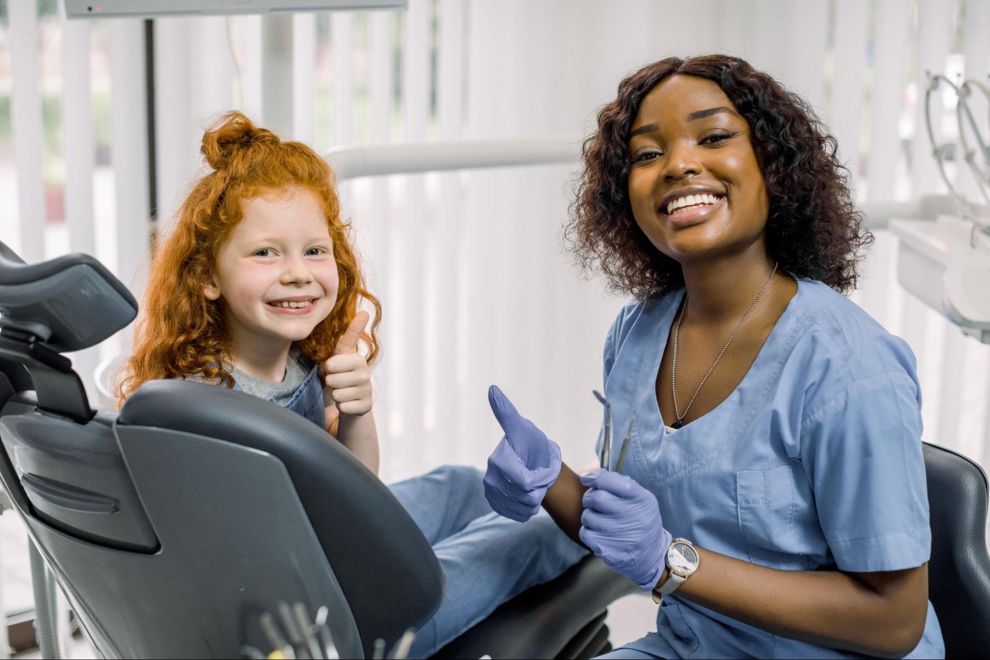Happy young girl in a dental exam chair next to a female dental professional.