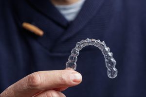 A smiling African American man with orthodontic braces, holding a plastic jaw model with metal brackets and another with invisible aligners.