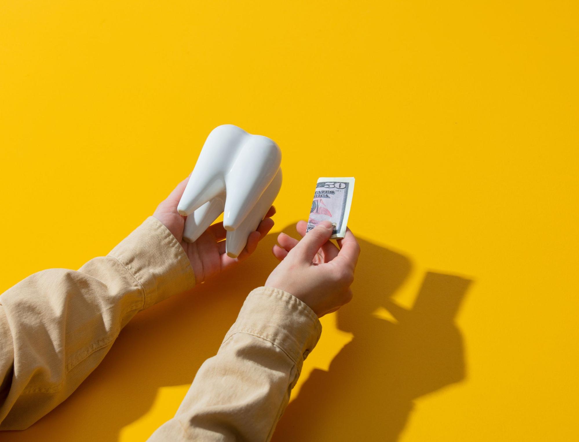 Person holding a tooth and money.