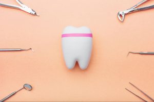 Dentist tools around a tooth model with a pink line against a peach background, symbolizing a tooth-filling procedure.
