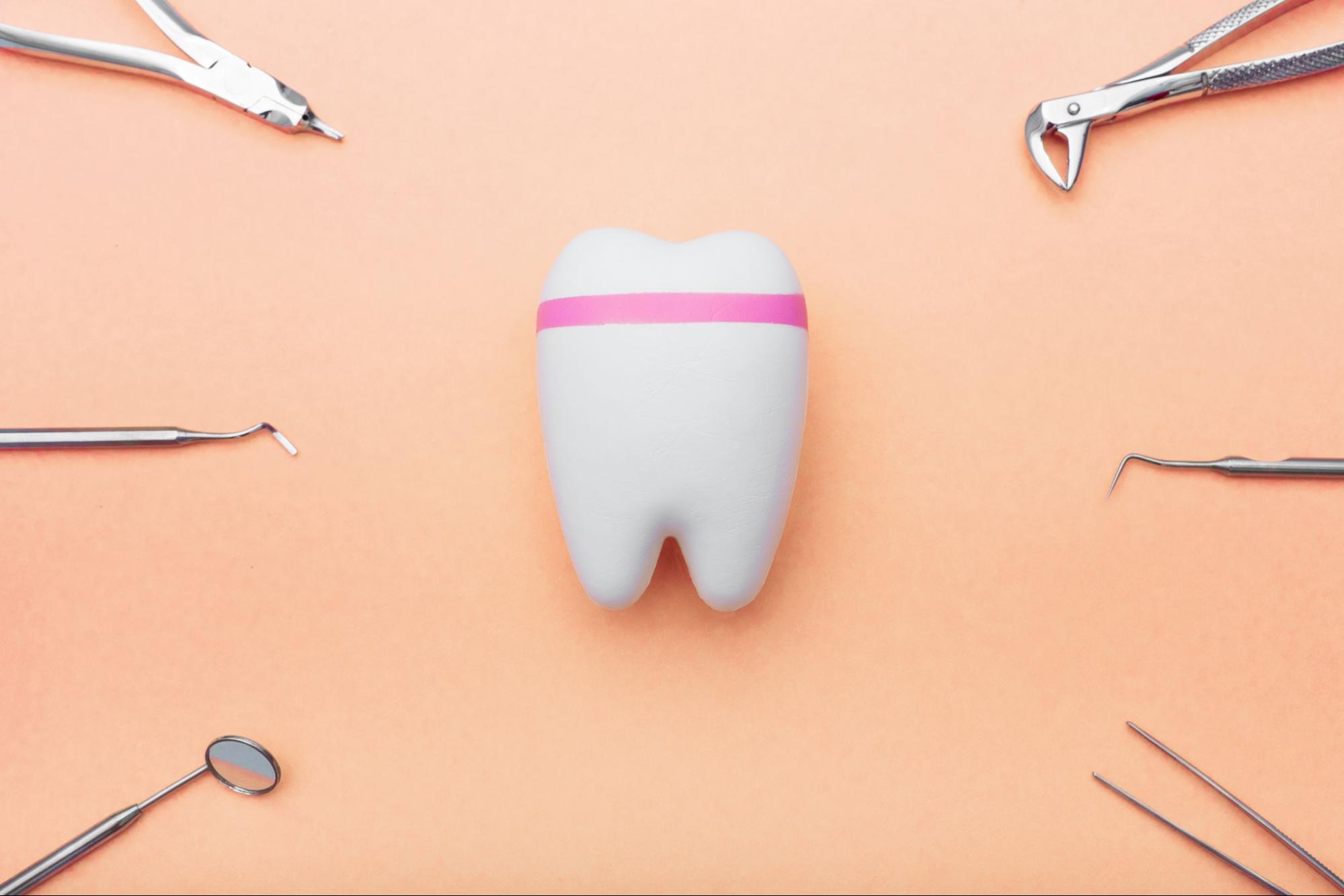 Dentist tools around a tooth model with a pink line against a peach background, symbolizing a tooth-filling procedure.