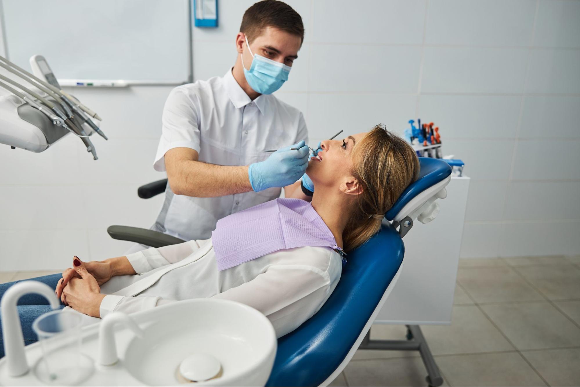 A male dentist conducts a thorough dental examination of a female patient’s teeth in a professional clinical setting.