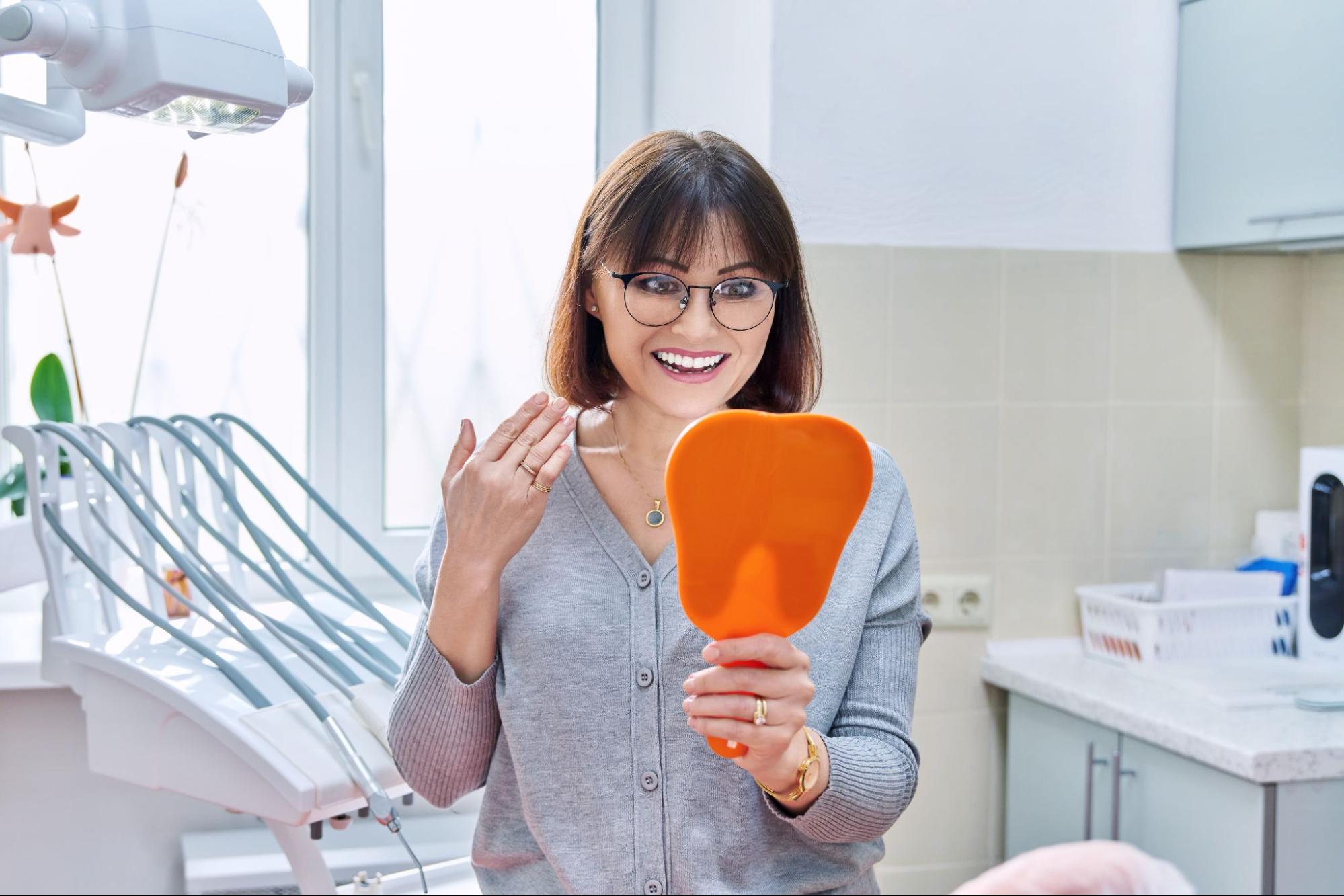Woman looking at her smile in a mirror at a dental office.