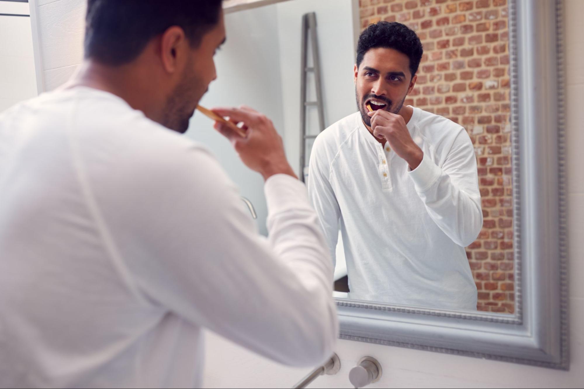 Man brushing his teeth and looking at himself in the mirror.