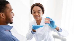 A female periodontist uses a teeth and jaw model to explain a patient's dental condition.