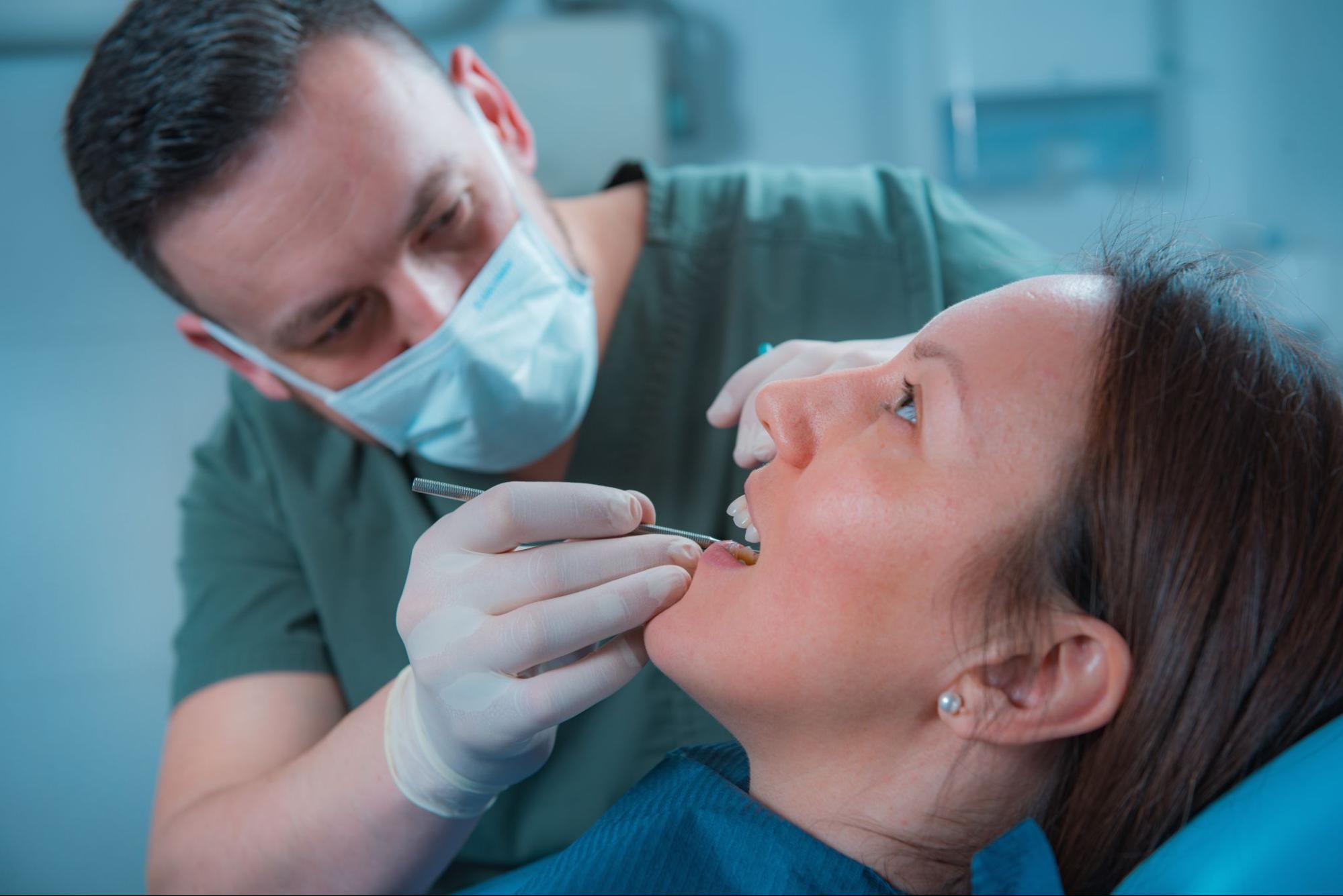 A male dentist inspects a female patient’s teeth in preparation for removing wisdom teeth.