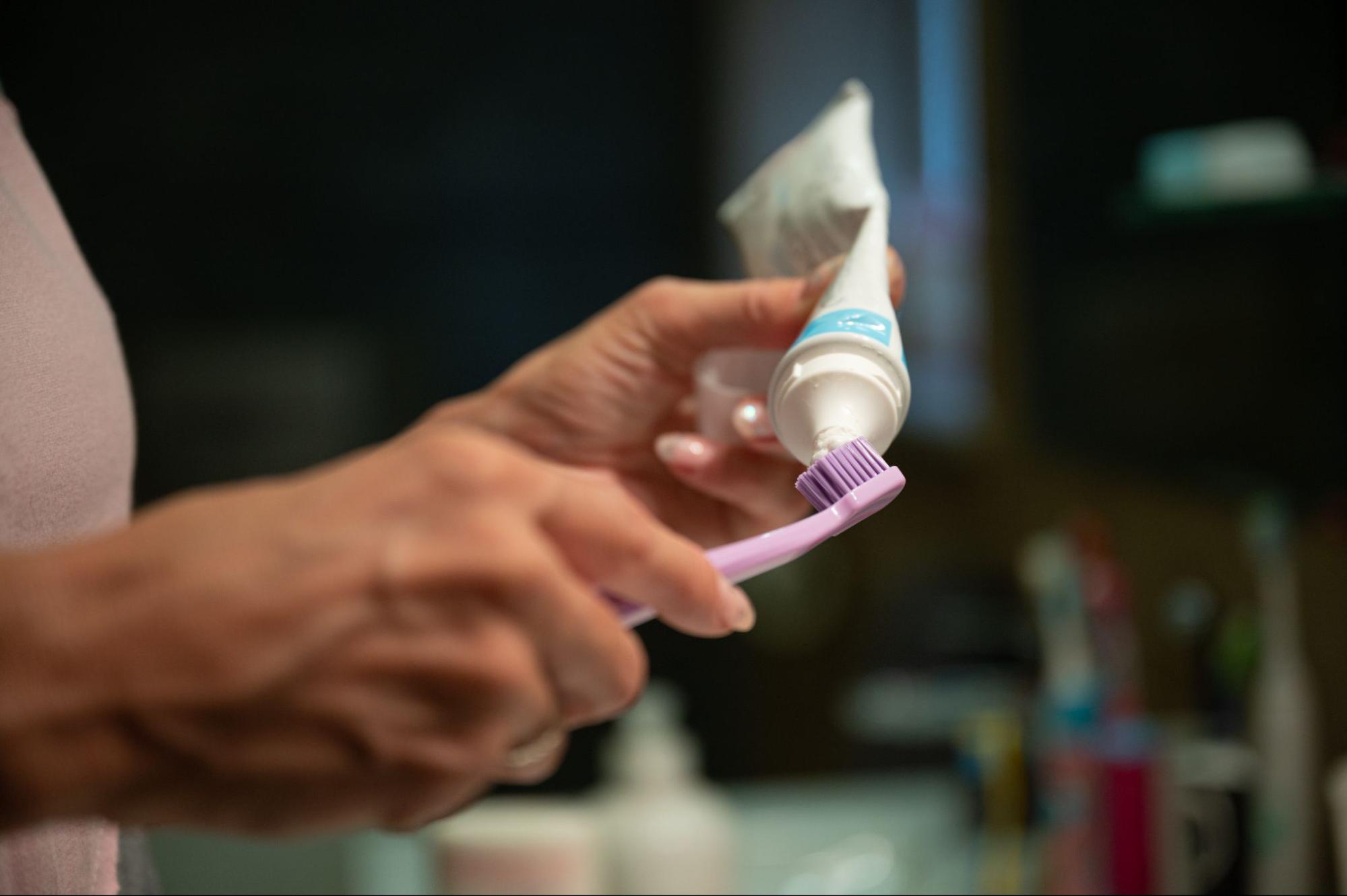 A close-up of hands applying toothpaste onto a toothbrush.