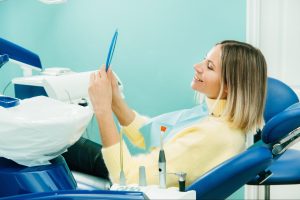 Woman in a dental exam chair looking at her teeth in a mirror.