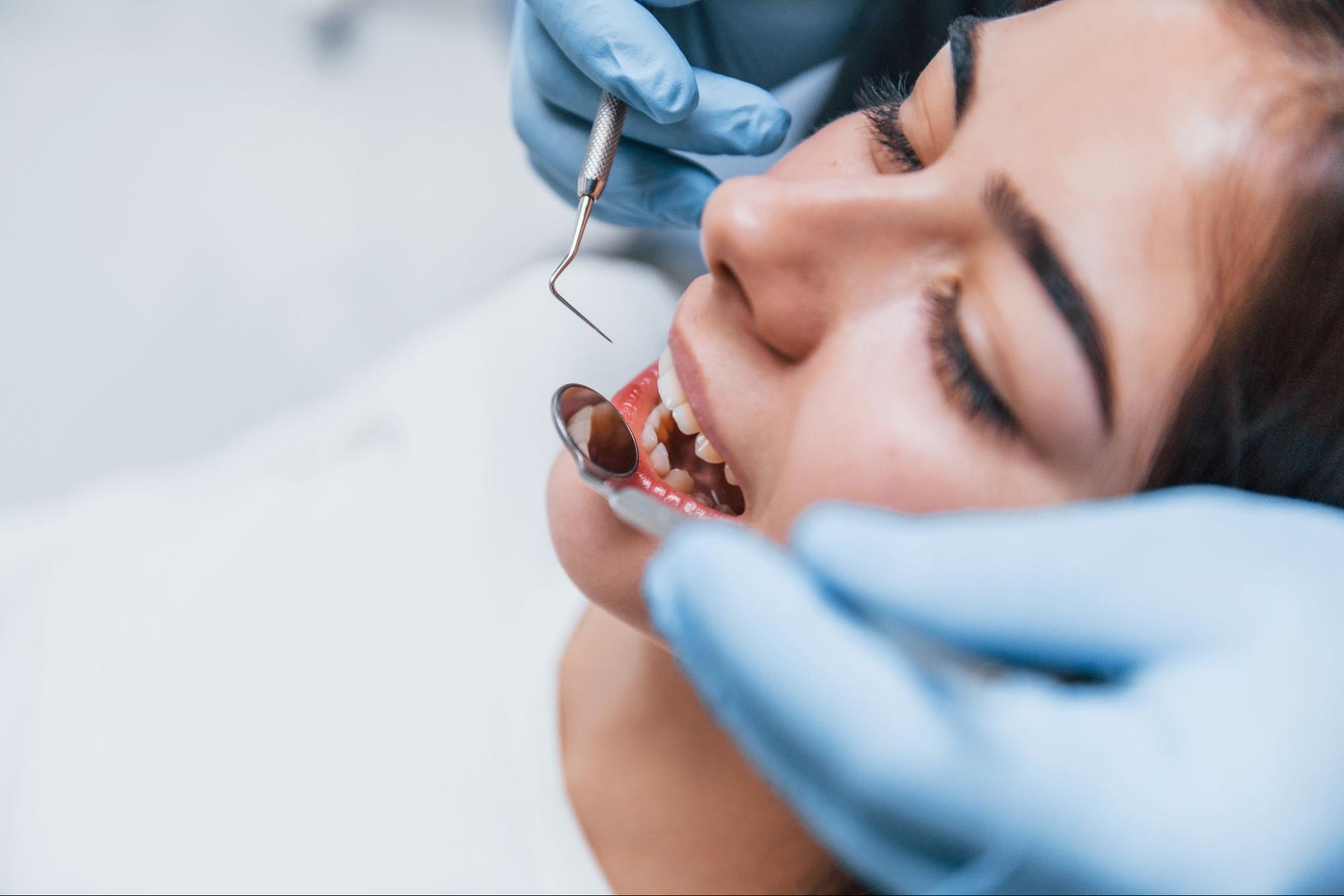 A close-up of a dentist examining a woman's teeth with dental tools before treatment.