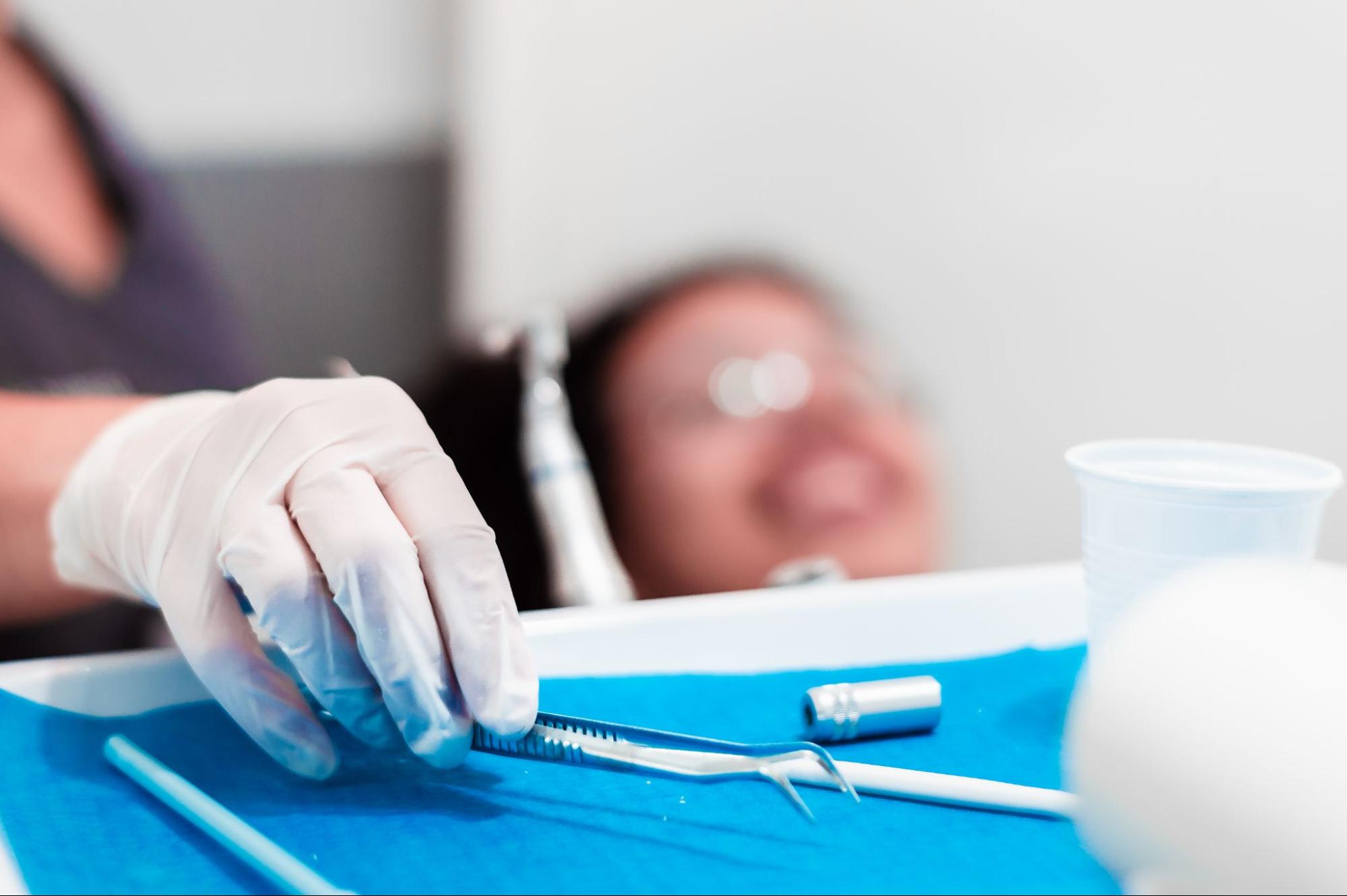 Gloved dentist holding a tool next to a patient.