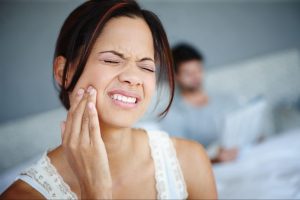 A woman grimaces in pain while holding her cheek due to a toothache.