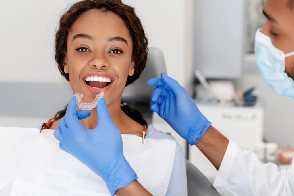 A cosmetic dentist fitting clear aligners on a female patient’s teeth