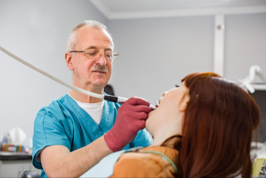 A senior general dentist performs dental treatment on a patient's tooth.