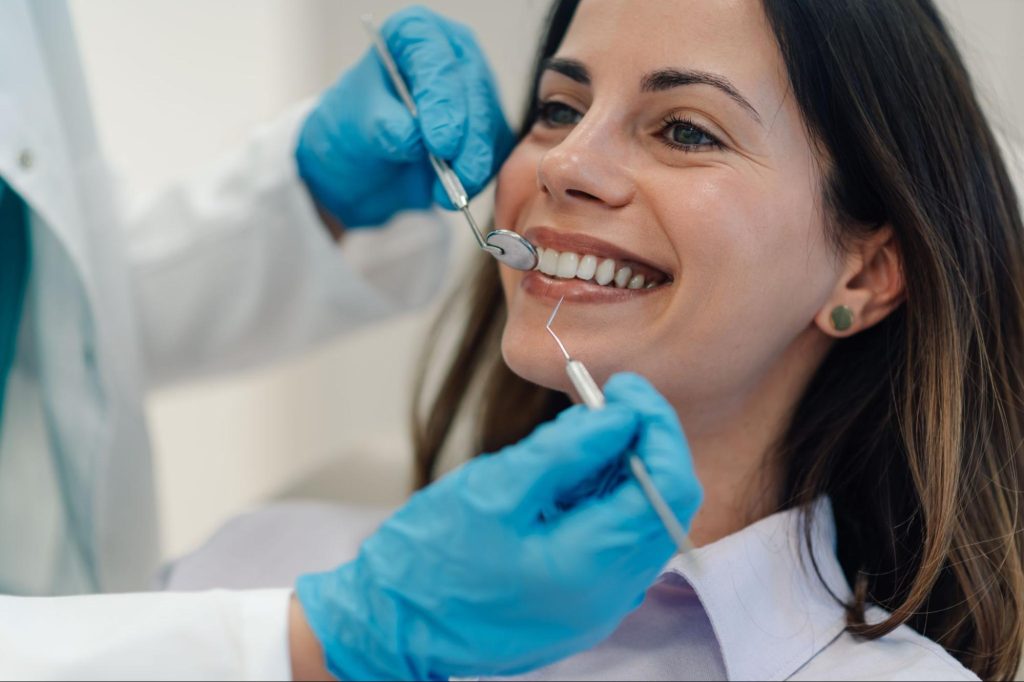 A female patient smiles as the dentist checks her teeth during a routine dental exam.