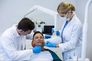 A general dentist examines a male patient using dental tools during a routine checkup.