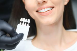 A close-up of a dentist’s hand matching the patient’s tooth shade with a color guide for cosmetic dental treatment.