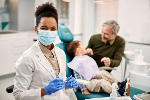 A female dentist standing in front of a child and their father.